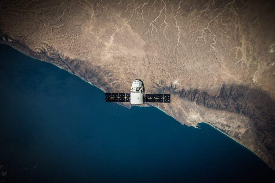 SpaceX Dragon capsule orbiting above Earth’s coastline with visible desert terrain and ocean view from space